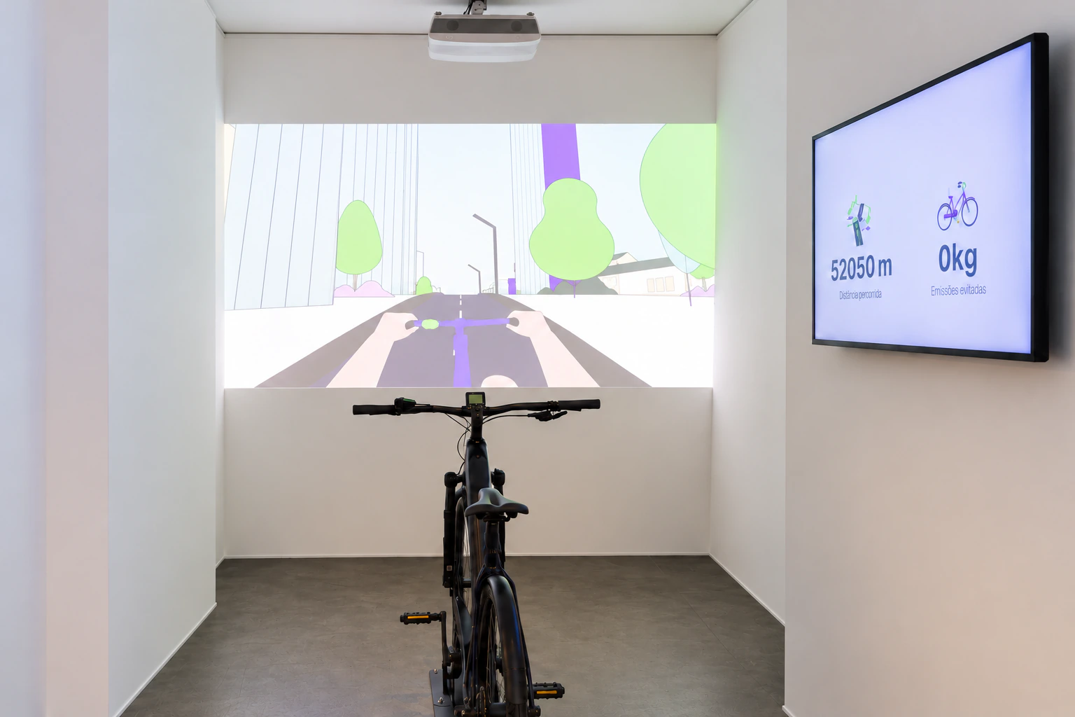 A bicycle faces a projected illustrated road in MAAT Central, beside a display of ride information.